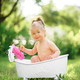 Happy toddler girl takes a milk bath with petals. Little girl in a milk  bath on a green background. Stock Photo by wolfhound9111