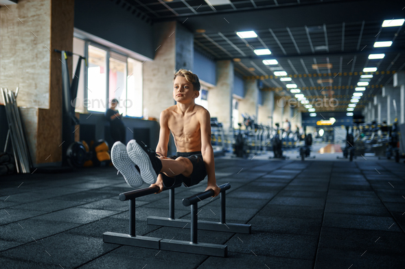 Boy doing ABS exercise on uneven bars in gym