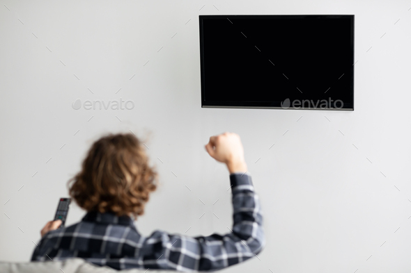 Guy Watching Sports On TV Sitting On Sofa Indoor, Back-View