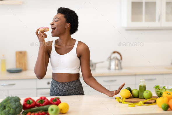 Black Female Enjoying Cheat Meal Eating Donut Posing In Kitchen