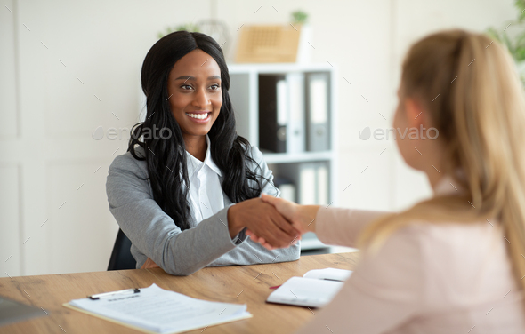 Unrecognizable black HR manager shaking hands with female job appicant on employment interview at