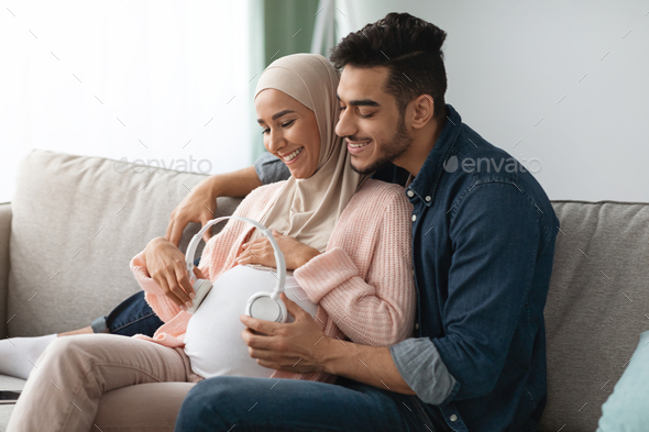 Pregnancy Music. Happy Pregnant Muslim Couple Placing Wireless Headphones On Woman\'s Belly