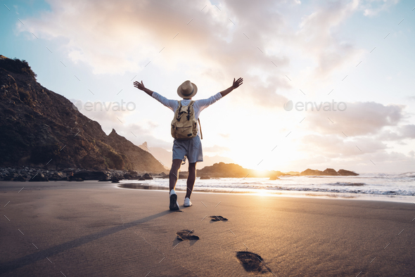 Young man arms outstretched by the sea at sunrise enjoying freedom and life