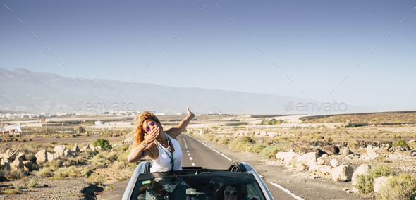 Beautiful traveler young woman send a kiss staying out of the roof of a convertible car