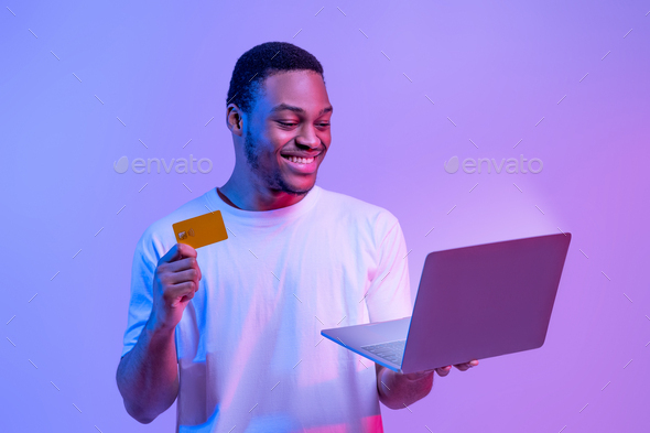 Online Payments. Happy african male with credit card and laptop, neon light