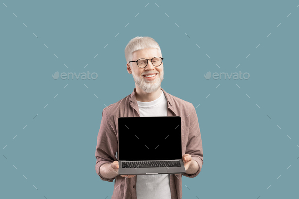 Smiling albino guy showing laptop computer blank screen to camera, standing over turquoise