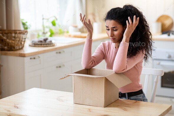 Wrong Parcel. Upset lady sitting with unpacked box in kitchen at home