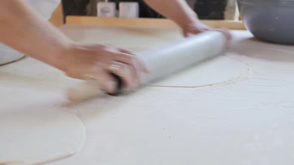 the Female Hands of the Baker Roll Out Thin Dough with a Rolling Pin on a Wooden Table for Baking alt