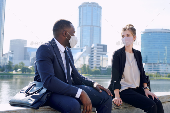 Two young intercultural business partners in formalwear and protective masks interacting at meeting - Stock Photo - Images