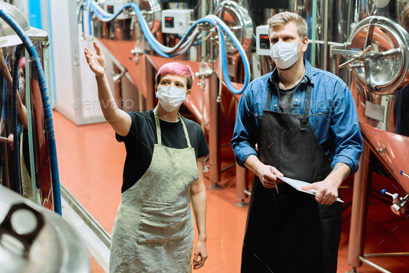 Two young brewers in protective masks discussing quality of new beer production equipment - Stock Photo - Images