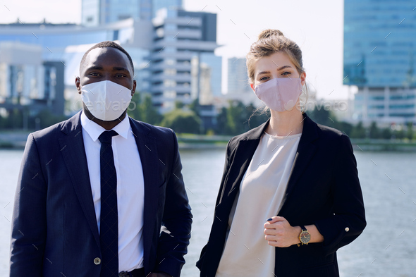 Two young intercultural managers in formalwear and protective masks standing against cityscape - Stock Photo - Images