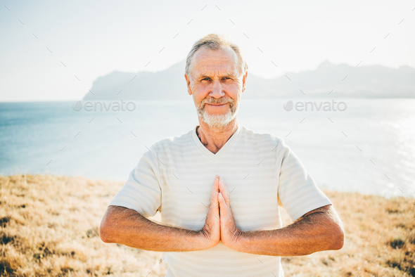 Close up portrait senior man doing yoga exercises at the mountain on the background. - Stock Photo - Images