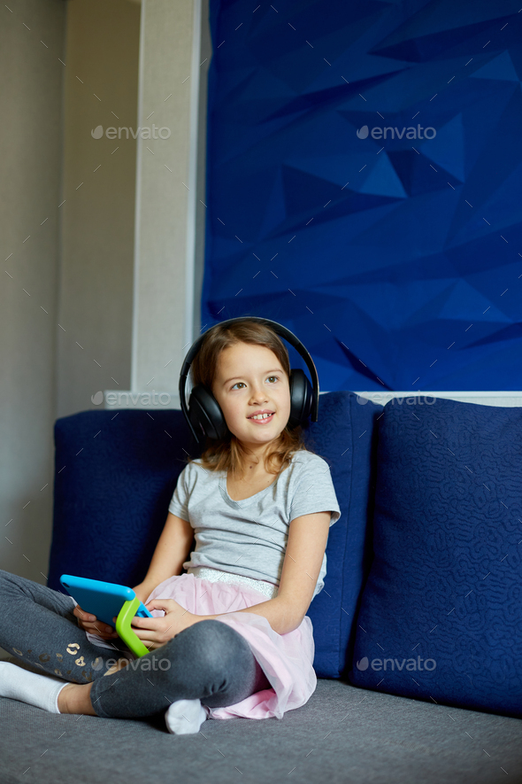 Premium Photo  Cute little girl sitting on couch, kid addicted to  technology, enjoying playing online game on digital tablet computer, using  applications, web surfing information at home