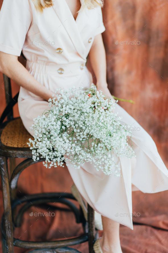 An unrecognizable woman in a beige dress holds a delicate bouquet of  gypsophila.