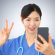 asian woman nurse takes a portrait picture on the phone doing the v sign - PhotoDune Item for Sale