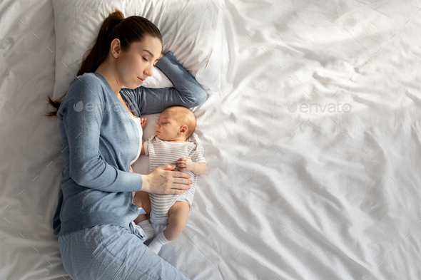 Co-sleeping with baby. Young woman napping in bed with her newborn child