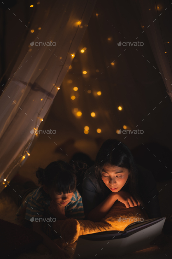 young Asian mother read the story in the book for her daughter children on the bed at home