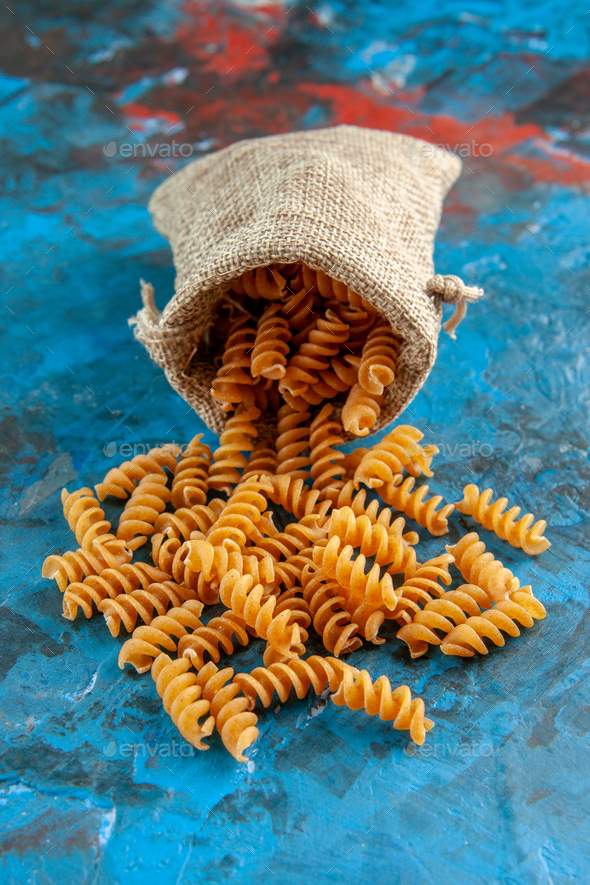 Vertical view of raw Italian pastas from the gray purse on blue background