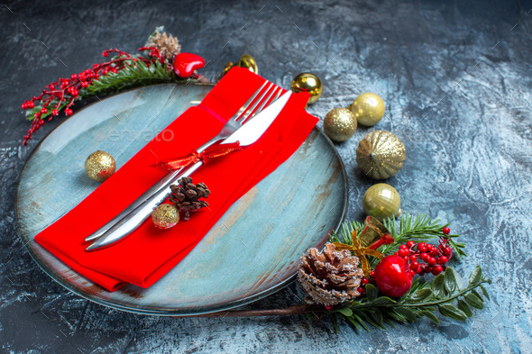 Side view of cutlery set with red ribbon on a decorative napkin on a blue plate and christmas