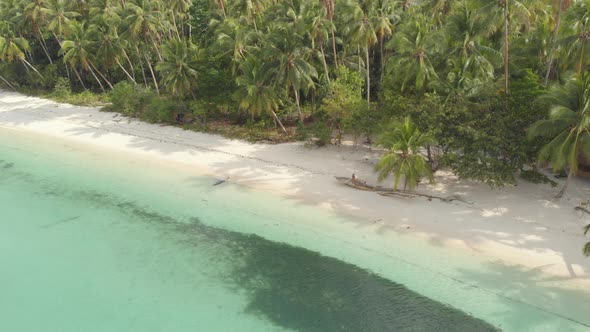 Aerial: woman relaxing on white sand beach turquoise water tropical Indonesia alt