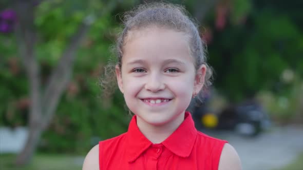 Funny Little Girl Smiles, Looking at the Camera on the Street, a Cute Child Plays on the Street alt