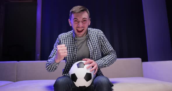 Caucasian Man Worried and Cheering Up for Football Game on TV Sitting on Sofa Late at Night