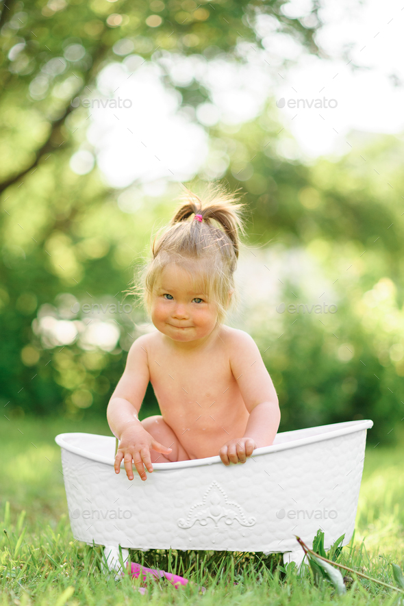 Happy toddler girl takes a milk bath with petals. Little girl in a milk  bath on a green background. Stock Photo by wolfhound9111