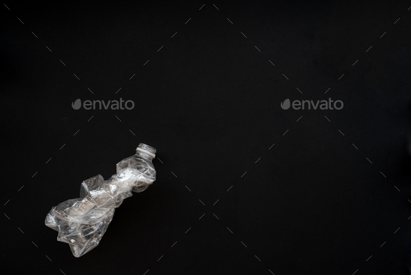 Compressed plastic bottle on a black background. The concept of saving the environment.