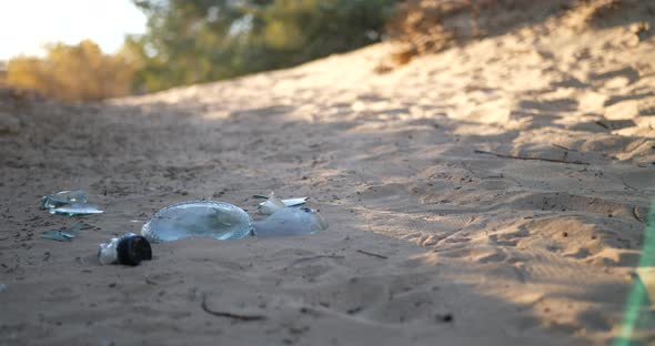 Low slide shot of a broken bottle, trash and litter on a natural dirt hiking trail at sunrise. alt