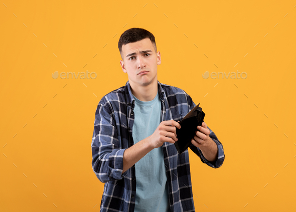 Bankruptcy concept. Upset young man showing empty wallet, suffering from loss of money on orange
