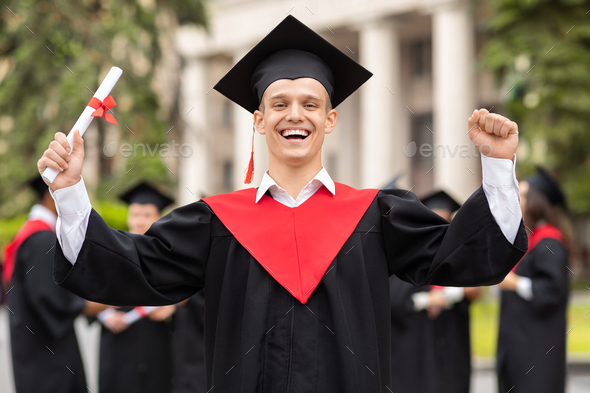 Delighted guy student having graduation party, raising hands up