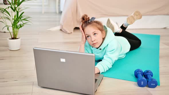 The Girl is Thinking and Looking for Sports Exercises in the Laptop