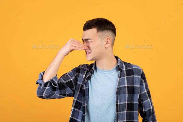 Cool millennial guy closing his nose, suffering from terrible smell, disliking bad odor on orange