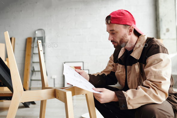 Contemporary furniture assemblage specialist looking through paper with instruction during work