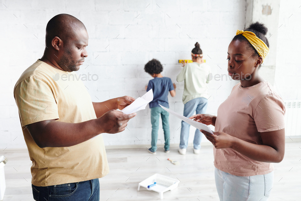 African man and woman in casualwear discussing papers with furniture assembling instructions