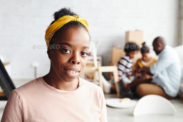 Happy African woman in yellow headband and beige t-shirt standing against her husband and children - Stock Photo - Images