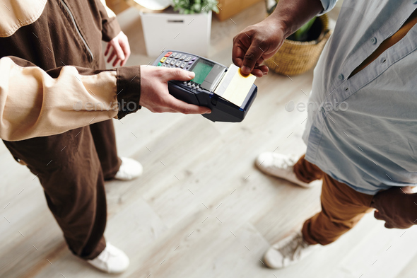 Hand of young man of African ethnicity paying for work of loaders while holding card over terminal - Stock Photo - Images