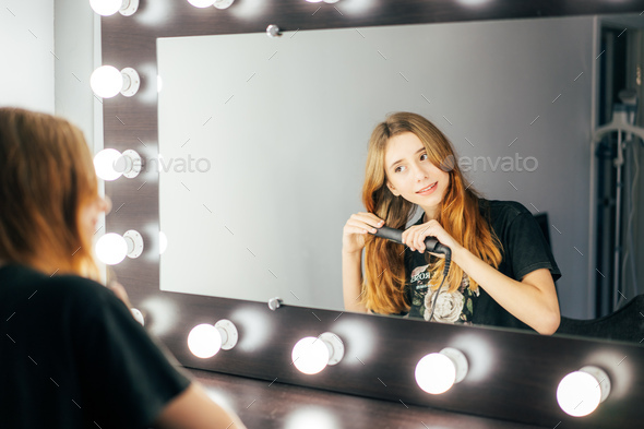 A Fifteen Year Old Teenage Girl Pulls Her Red Wavy Hair With A Hair Straightener Stock Photo By Titovailona