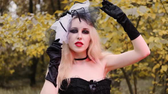 A beautiful girl in the image of a witch in black gloves with black eyes and red lips. Halloween, au alt