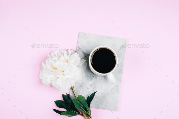 Coffee mug, notebook and white peony flowers on pink background. Cozy, still life, minimal concept