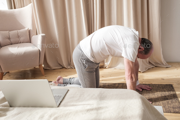 Senior man working out at home in living room, doing yoga exercise on mat. - Stock Photo - Images