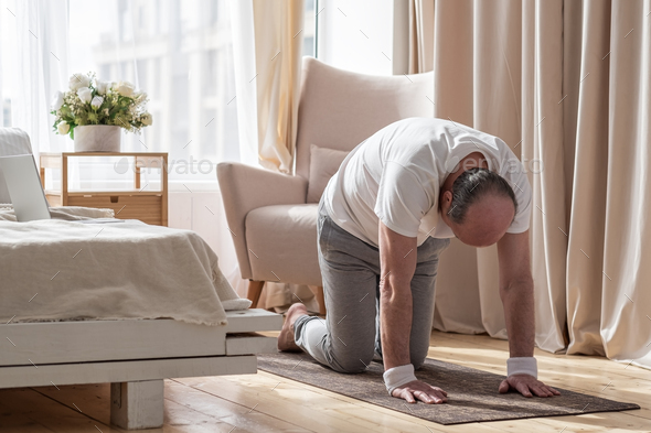 Senior man working out at home in living room, doing yoga exercise on mat. - Stock Photo - Images