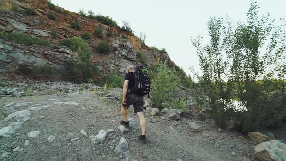 traveler in comfortable clothes and in running shoes is walking at the edge of a river alt