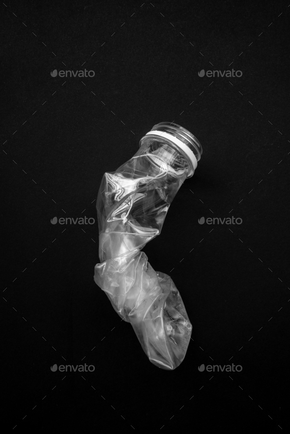 Compressed plastic bottle on a black background. The concept of saving the environment.