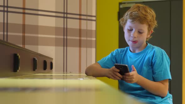 Blonde boy uses smartphone while surfing the internet in cafe alt