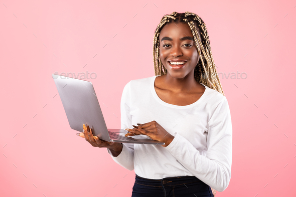 Smiling young black lady holding and using laptop at studio