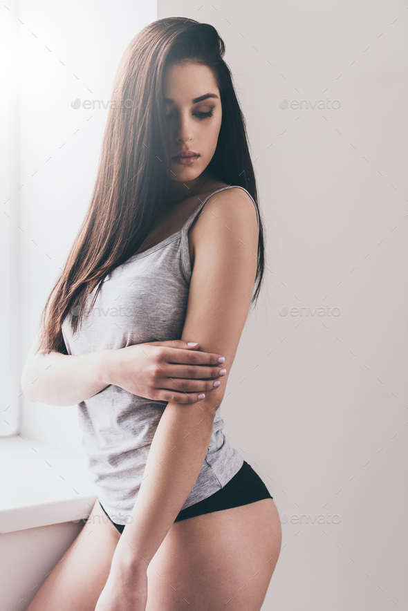 Pure beauty. Beautiful young woman in panties and tank top standing near  the window and looking away Stock Photo by gstockstudio