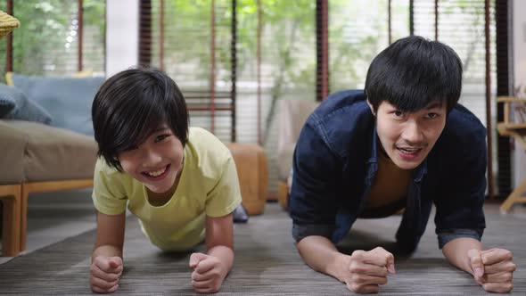 Asian father and son compete in plank exercise together at home. alt