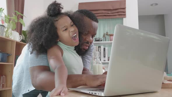 African American dad and daughter culinary lesson online with laptop at the home kitchen table