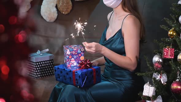 Young Woman in a Medical Mask and Evening Dress Holds Sparklers in Her Hand While Sitting Near a